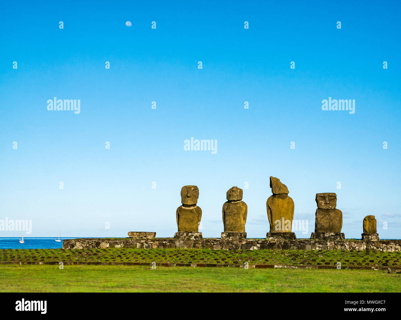Ahu Vai Ura, Tahai Moai figure, Hanga Roa, Isola di Pasqua, Cile, con la luna nel cielo blu durante il giorno e yacht ancorati in Oceano Pacifico Foto Stock