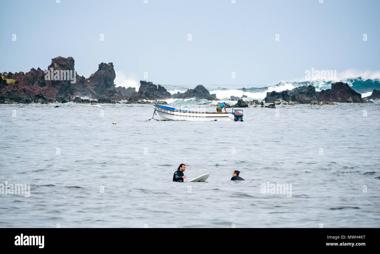 Surfers in attesa di onda con barca e subacquei e grande onda rompe sulla costa rocciosa, Hanga Roa, Isola di Pasqua, Rapa Nui, Cile Foto Stock