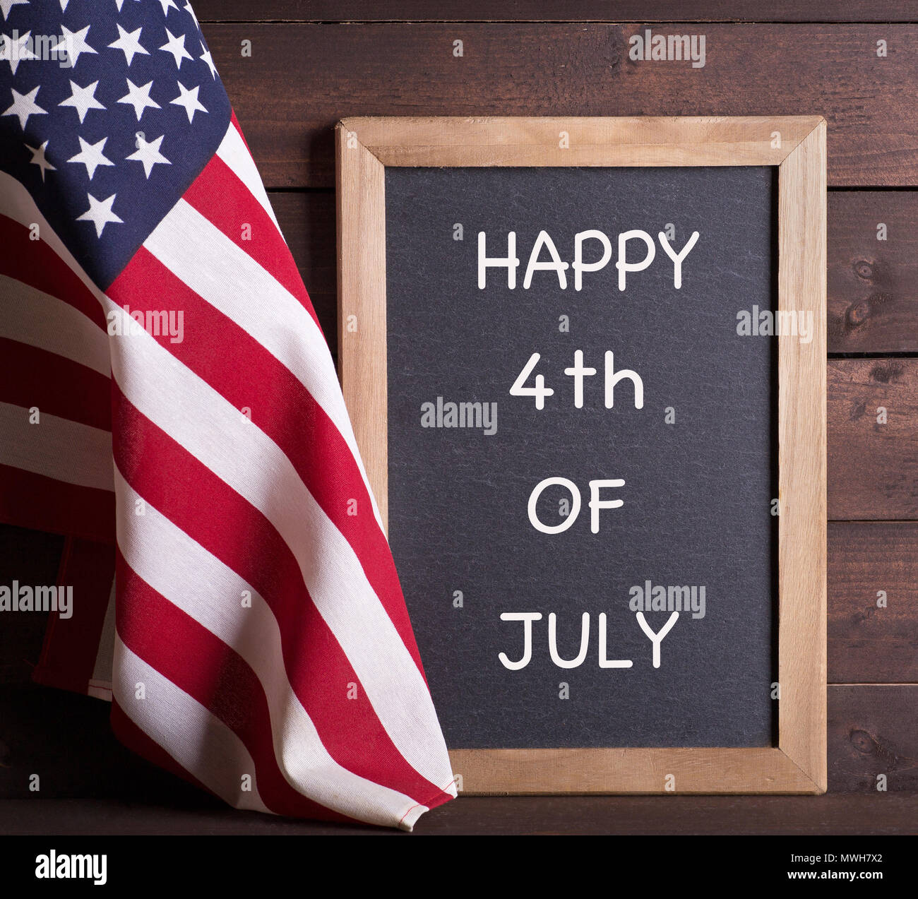 Bandiera americana con felice 4 di luglio scritto su una lavagna su un rustico sfondo di legno Foto Stock