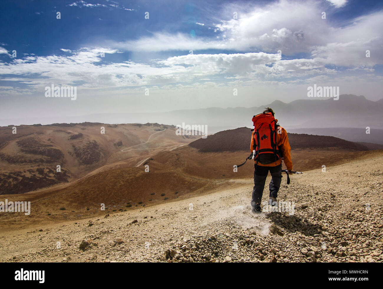 Uomo con zaino sul percorso nel deserto vicino neide vulcano sull isola di Tenerife con pietre e cielo blu e nuvole sotto Foto Stock