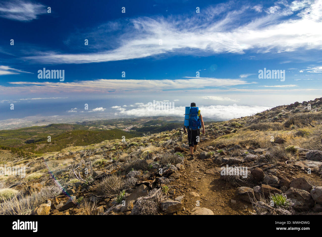 Uomo con zaino sul percorso in semidesert vicino neide vulcano sull isola di Tenerife con pietre e cielo blu e nuvole sotto Foto Stock