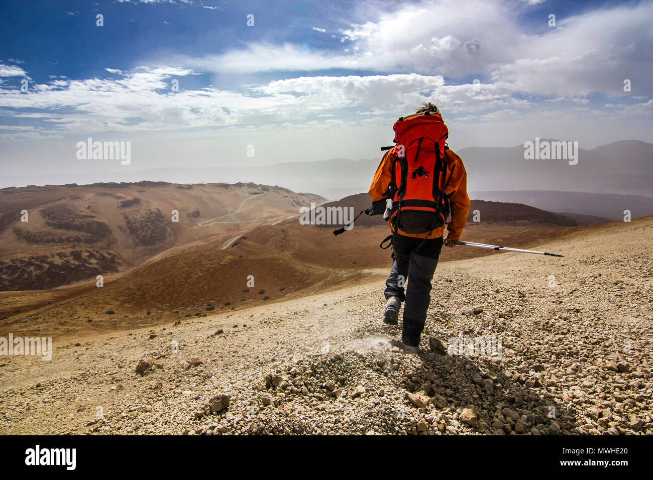 Uomo con zaino sul percorso nel deserto vicino neide vulcano sull isola di Tenerife con pietre e cielo blu e nuvole sotto Foto Stock