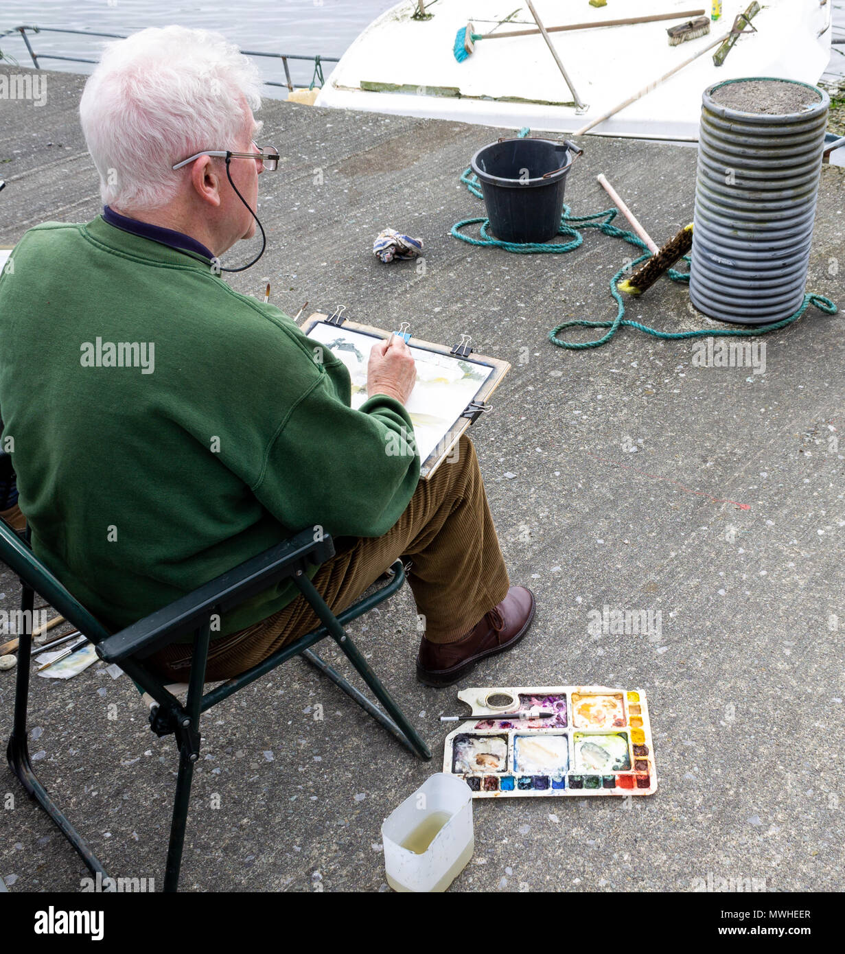 artista maschile seduto su una banchina dipingere il paesaggio locale con i colori dell'acqua. Foto Stock