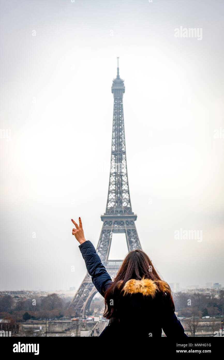 Giovane turista facendo V di vittoria di fronte alla Torre Eiffel, Parigi, Francia Foto Stock