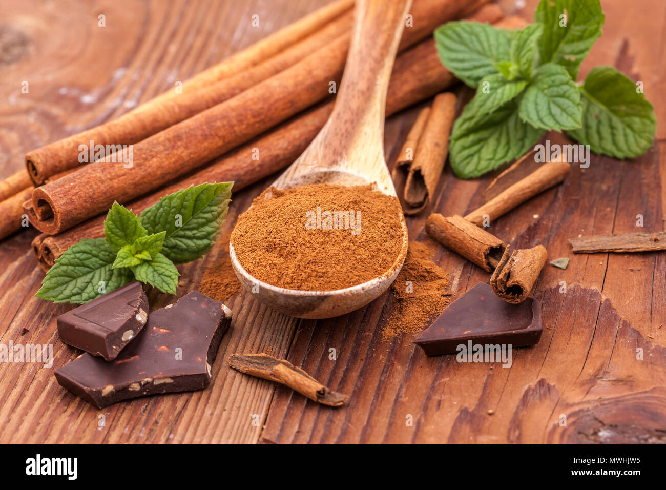 Cannella in polvere su un cucchiaio di legno, foglie di menta, bastoncini di  cannella, e pezzetti di cioccolato fondente Foto stock - Alamy