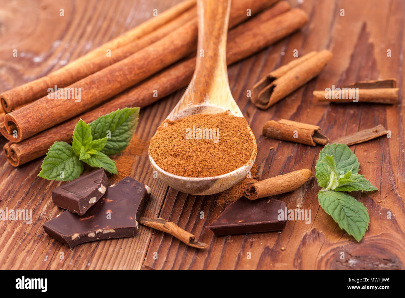 Cannella in polvere su un cucchiaio di legno, foglie di menta, bastoncini di cannella, e pezzetti di cioccolato fondente. Foto Stock