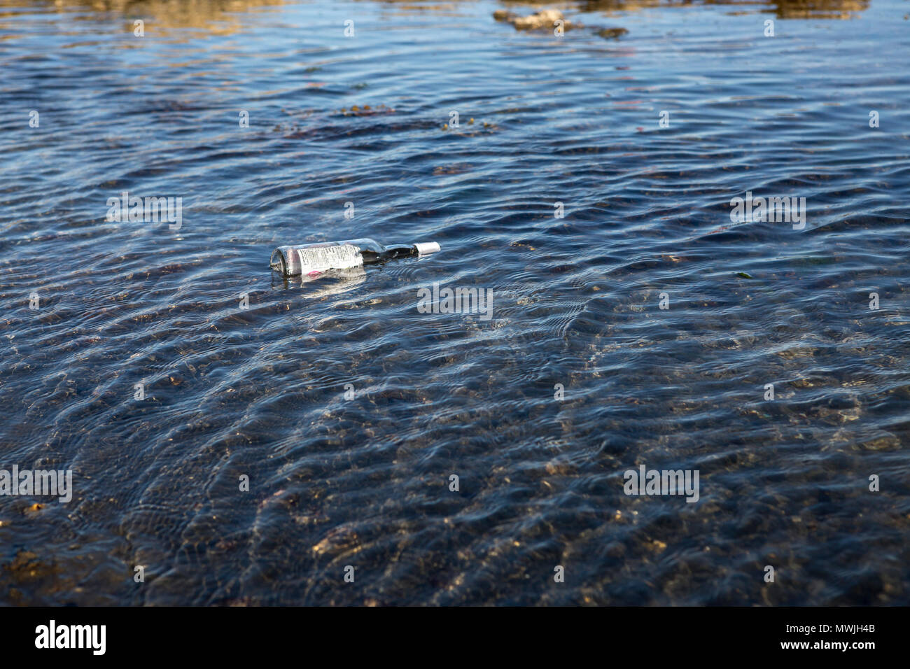 Alcol vuota bottiglia di vetro galleggiante in acqua di mare increspato Foto Stock