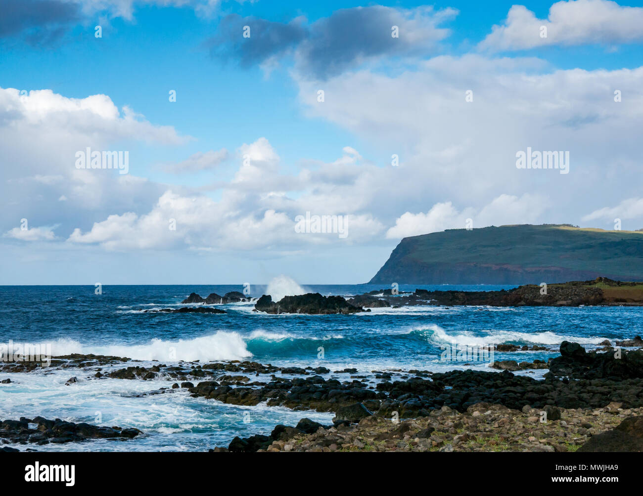 Oceano onde che si infrangono sulla spiaggia rocciosa, costa sud dell'isola di pasqua, Rapa Nui, Cile, con vista del vulcano estinto Rano Kau Foto Stock
