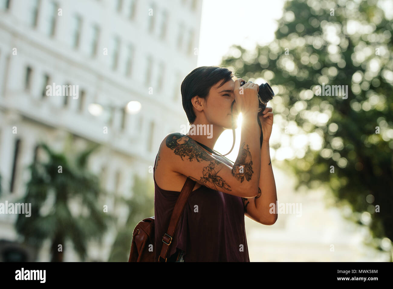Donna traveler prendendo foto utilizzando la sua fotocamera con Sun in background. Turistico con tatuaggio sulla sua mano andando in giro per la città prendendo fotografie. Foto Stock