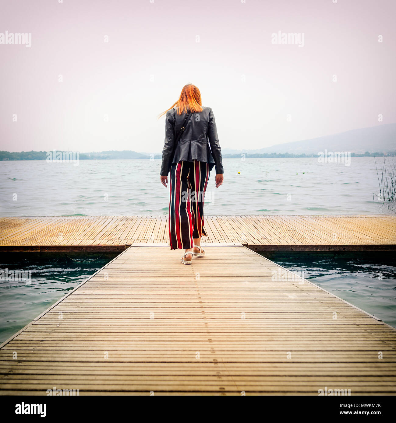 Giovane donna camminando sul molo verso il lago, il Lago di Pusiano, Lecco, Italia Foto Stock