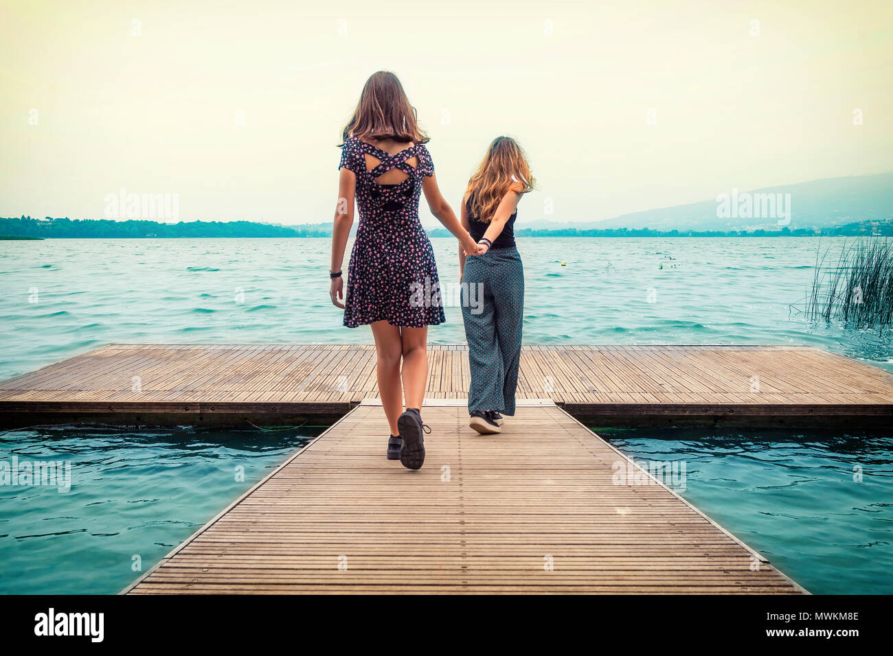Due giovani sorelle sulla banchina a camminare verso il lago, lago di Pusiano, Lecco, Italia Foto Stock
