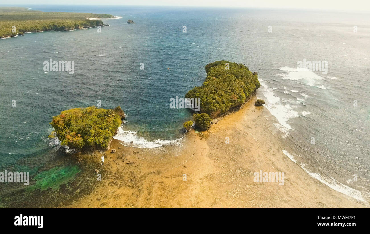 Vista aerea: mare e l'isola tropicale con rocce, la spiaggia e le onde. Costa dell'isola tropicale Siargao con le montagne e la foresta pluviale su uno sfondo di oceano con grandi onde. Seascape: sky, nuvole oceano. Filippine. Concetto di viaggio. Foto Stock
