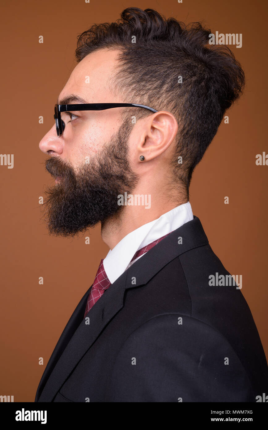 Giovane bello barbuto imprenditore persiano contro backgro marrone Foto Stock