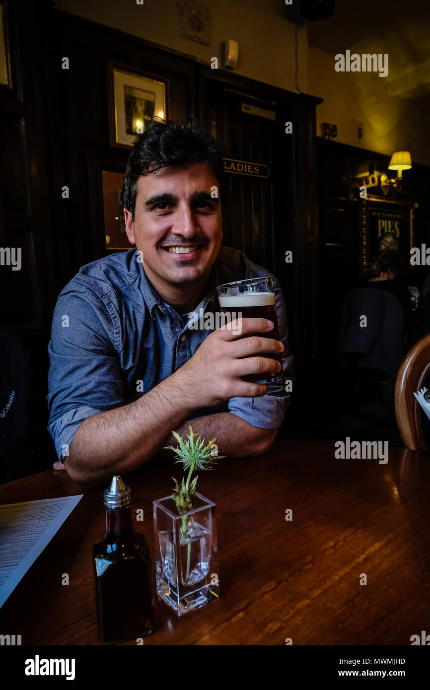 Uomo brasiliano tenendo la pinta di birra scura e prendendo un sorso in un tradizionale pub inglese, Edimburgo, Scozia Foto Stock