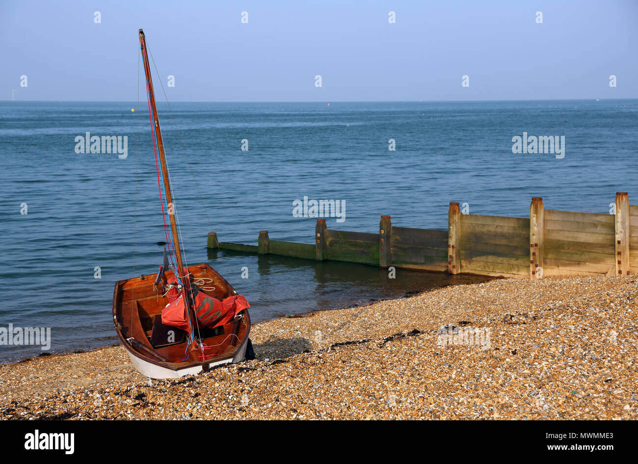 Un rosso e bianco dinghy in appoggio sulla spiaggia di ciottoli a Whitstable, Kent, Regno Unito. Foto Stock
