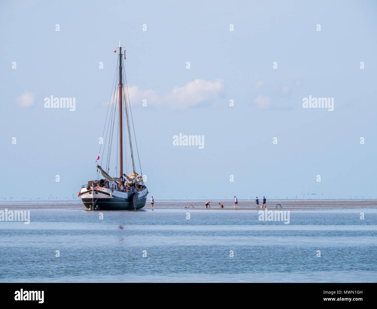 Un gruppo di ragazzi giocare sulla sabbia piatta e asciugata a fondo piatto yacht a vela a bassa marea sul mare di Wadden, Paesi Bassi Foto Stock