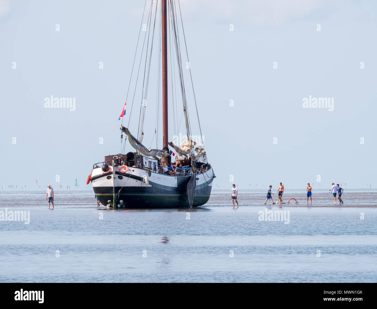 Un gruppo di ragazzi giocare sulla sabbia piatta e asciugata a fondo piatto yacht a vela a bassa marea sul mare di Wadden, Paesi Bassi Foto Stock