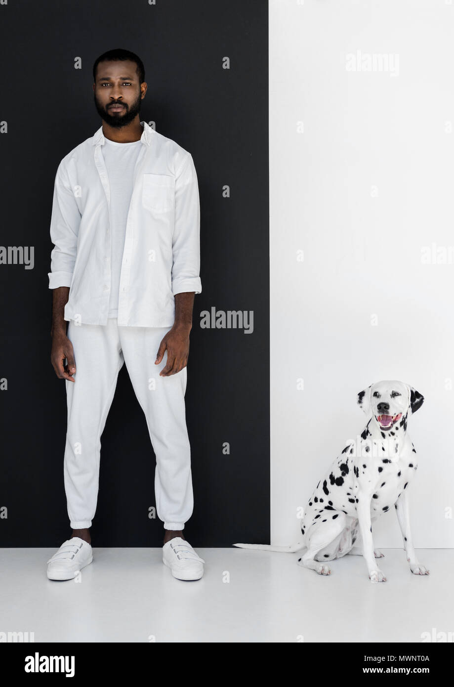 Bello stile americano africano uomo in bianche vesti e cane dalmata in  piedi vicino al nero e muro bianco Foto stock - Alamy