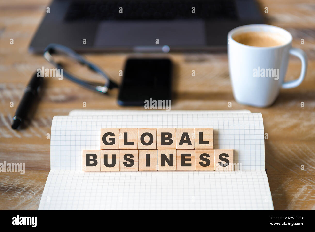 Primo piano su notebook su tavola di legno sfondo, concentrarsi sui blocchi di legno con lettere Making Global Business testo. Foto Stock