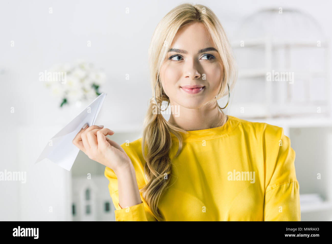 Trasognata imprenditrice in giallo camicetta holding aeroplano di carta Foto Stock