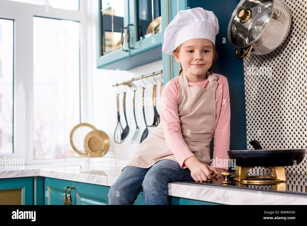 Carino bambino sorridente in chef hat e grembiule guardando padella sulla stufa Foto Stock