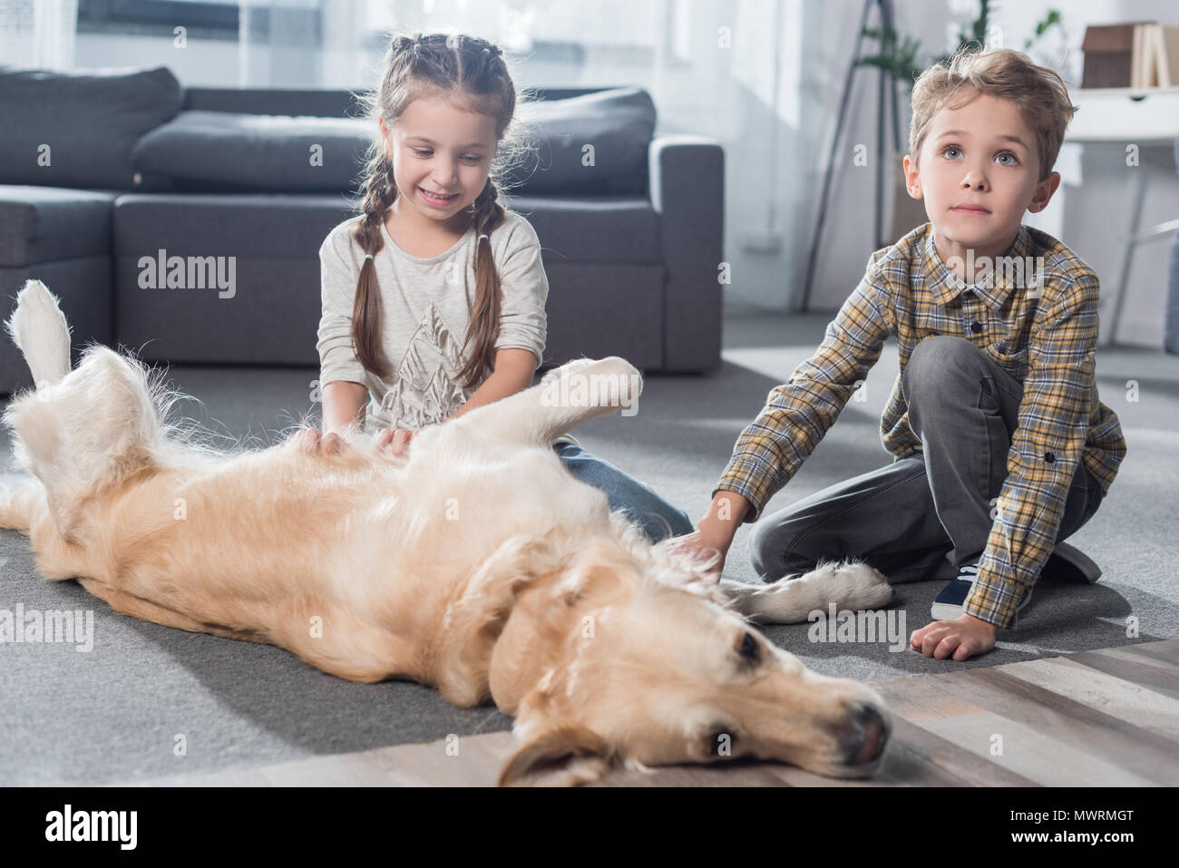 Piccolo Ragazzo e ragazza che gioca con il loro cane sul pavimento nel soggiorno Foto Stock