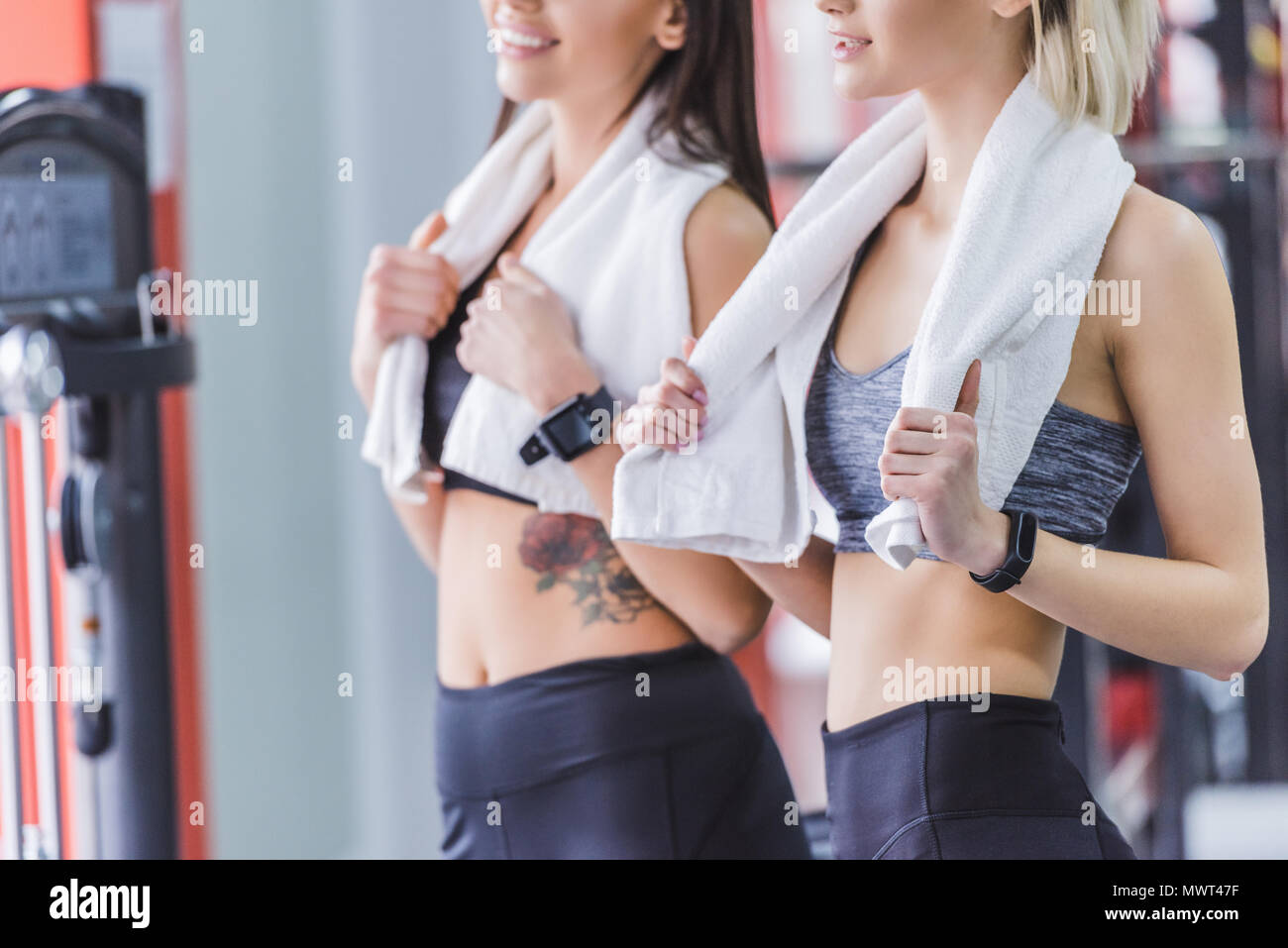 Ritagliato colpo di donne sportive con asciugamani e smart orologi rilassante dopo la formazione presso la palestra Foto Stock