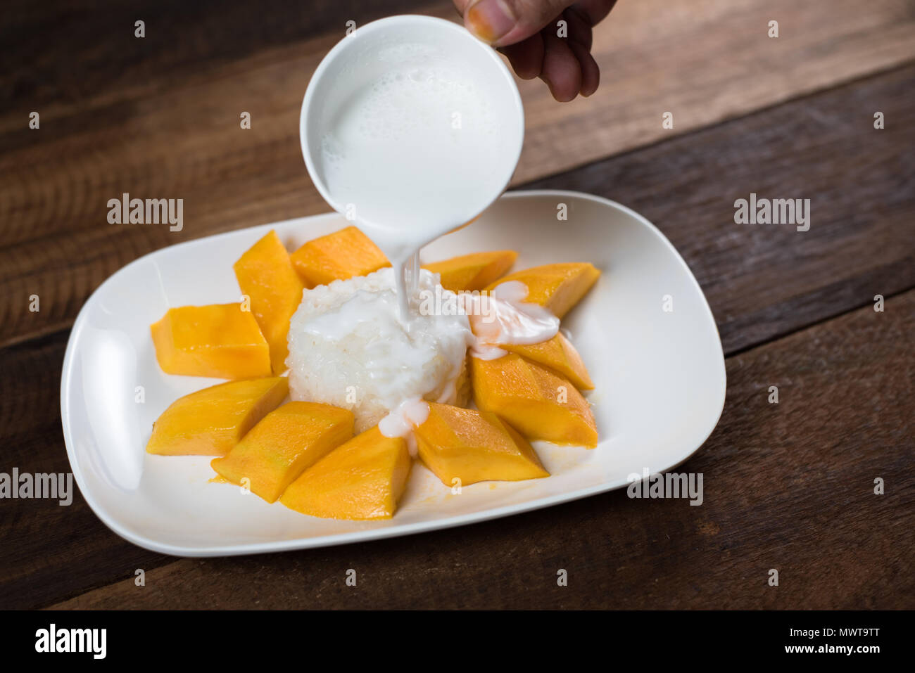 Versare il latte cocunut sul mango riso appiccicoso, un tradizionale dessert in Thailandia il cibo e la gastronomia concept Foto Stock