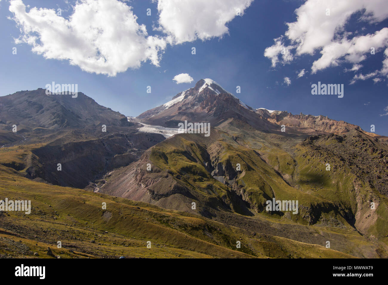 Kazbek Mountain in Georgia al tramonto con le nuvole in cielo ed erba sulle colline Foto Stock
