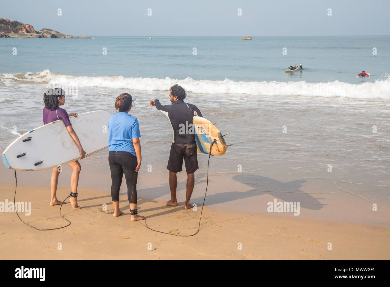 Gli studenti di Surf salire in acqua in una spiaggia a Goa, India, durante un inizio sessione estiva. Foto Stock