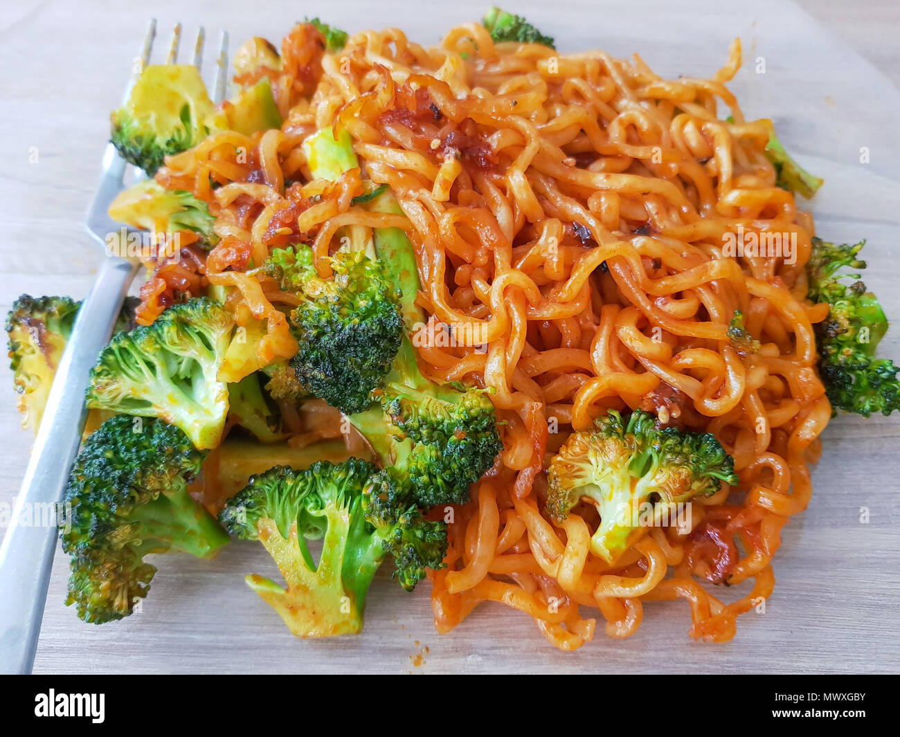 Vista dall'alto. Yummy. Il coreano piccante tagliatelle istante con vegetali verdi, broccoli sulla piastra con la forcella sulla tavola di legno con luce naturale dello sfondo. Foto Stock