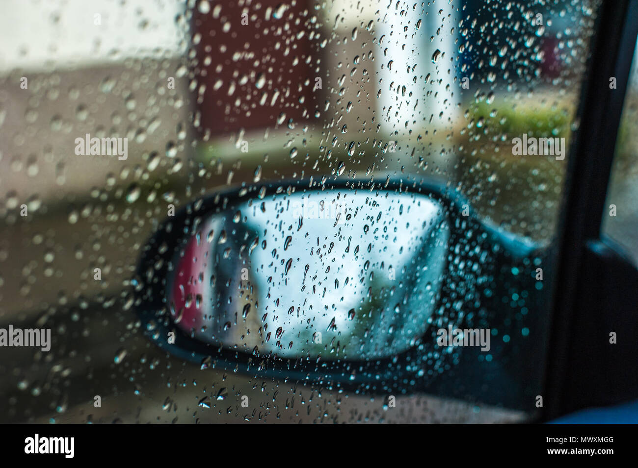 Vista del lato macchina specchio attraverso il vetro della finestra della macchina coperto da gocce di pioggia Foto Stock