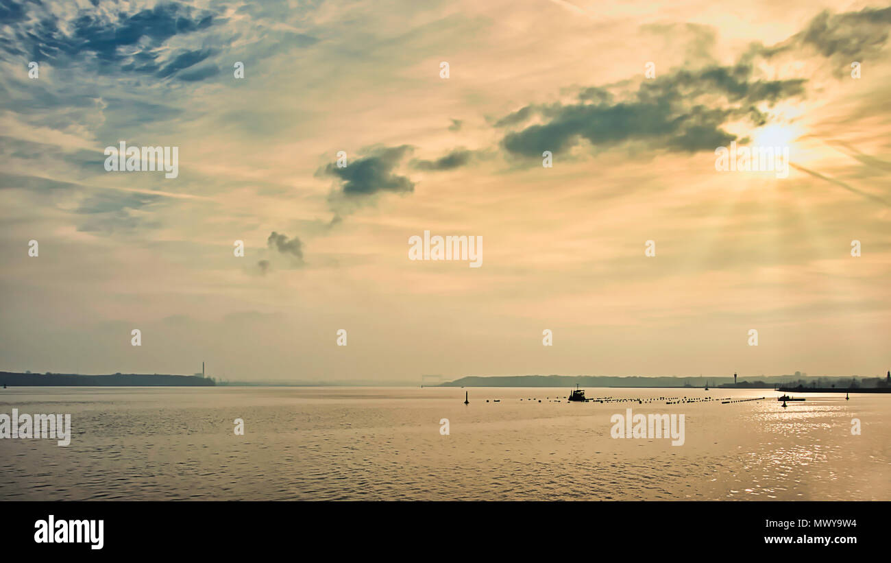 Seehafen Kiel, Nord-Ostsee-Kanal, Germania. Deutschland. Fiordo di Kiel incontra il fiume Eider estuario e ingresso al canale di Kiel. Il sole brilla luminosa attraverso un sottile haze di nuvole che illumina il mare sotto nella luce calda del sole. Fotografato in sun. Le masse di terra sono eseguite lungo l'orizzonte. Foto Stock