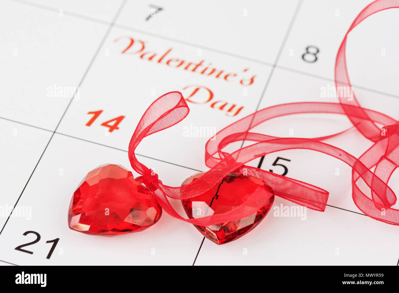 Due rosso trasparente cuori con scarlatto nastri sul calendario con l'iscrizione il giorno di San Valentino. Sfondo di un biglietto di auguri per San Valenti Foto Stock