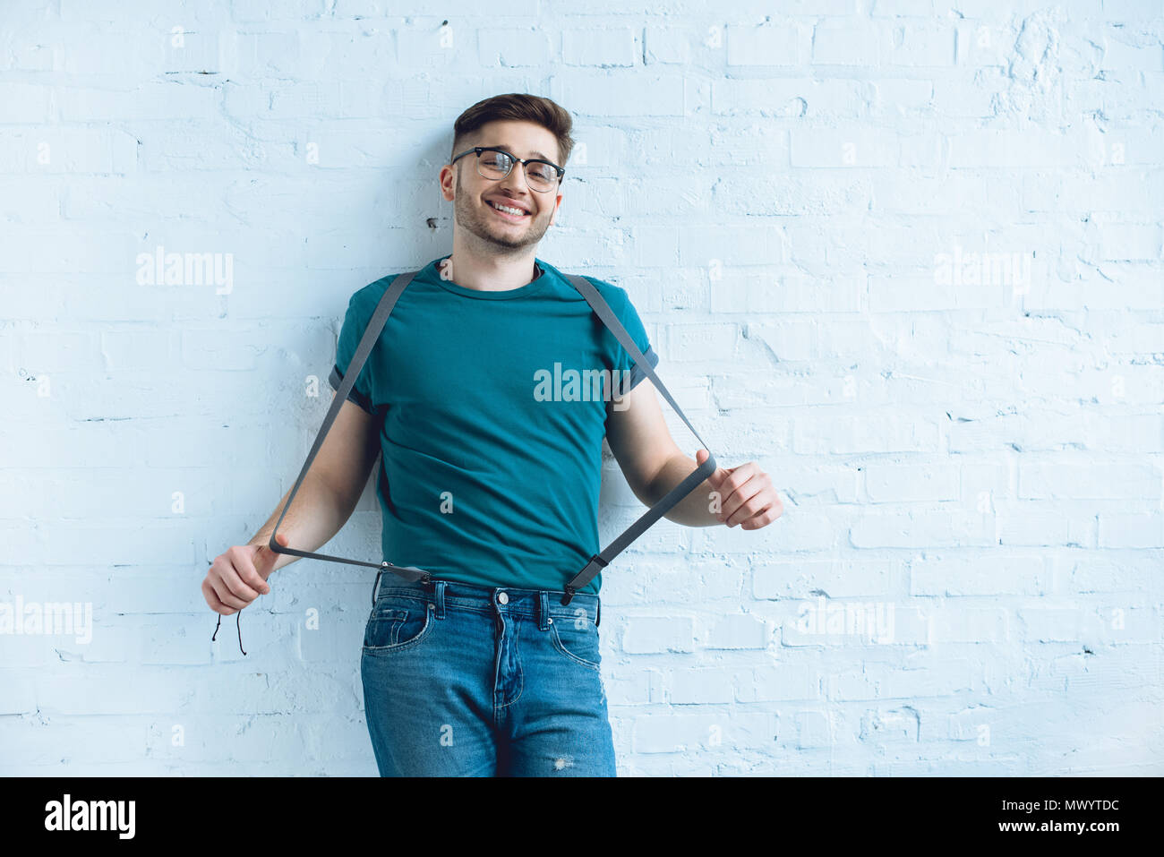 Sorridente uomo barbuto che indossa jeans con bretelle di fronte a un muro  di mattoni Foto stock - Alamy