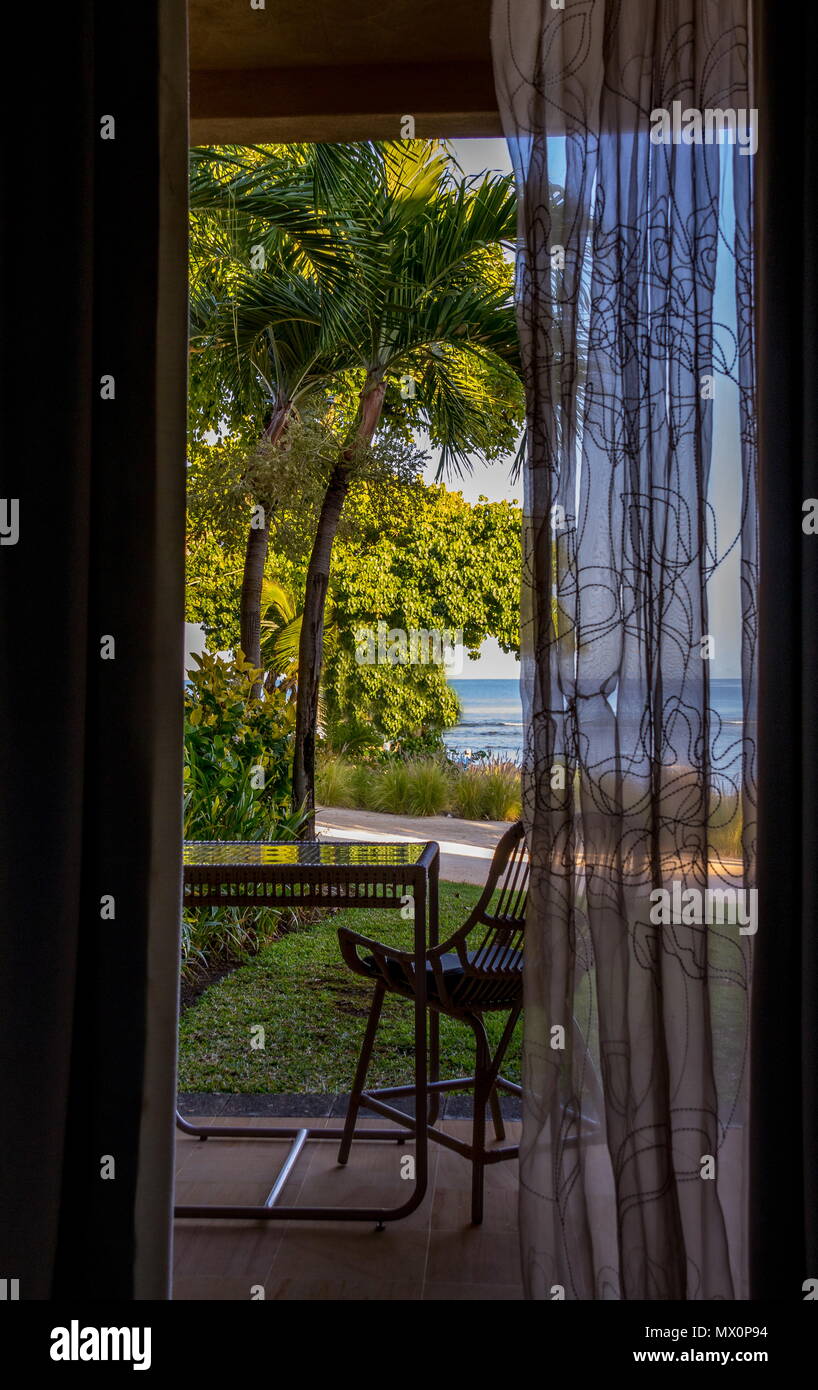 Vista di un mare tropicale spiaggia attraverso una porta aperta con una tenda di pizzo immagine con spazio copia in formato verticale Foto Stock