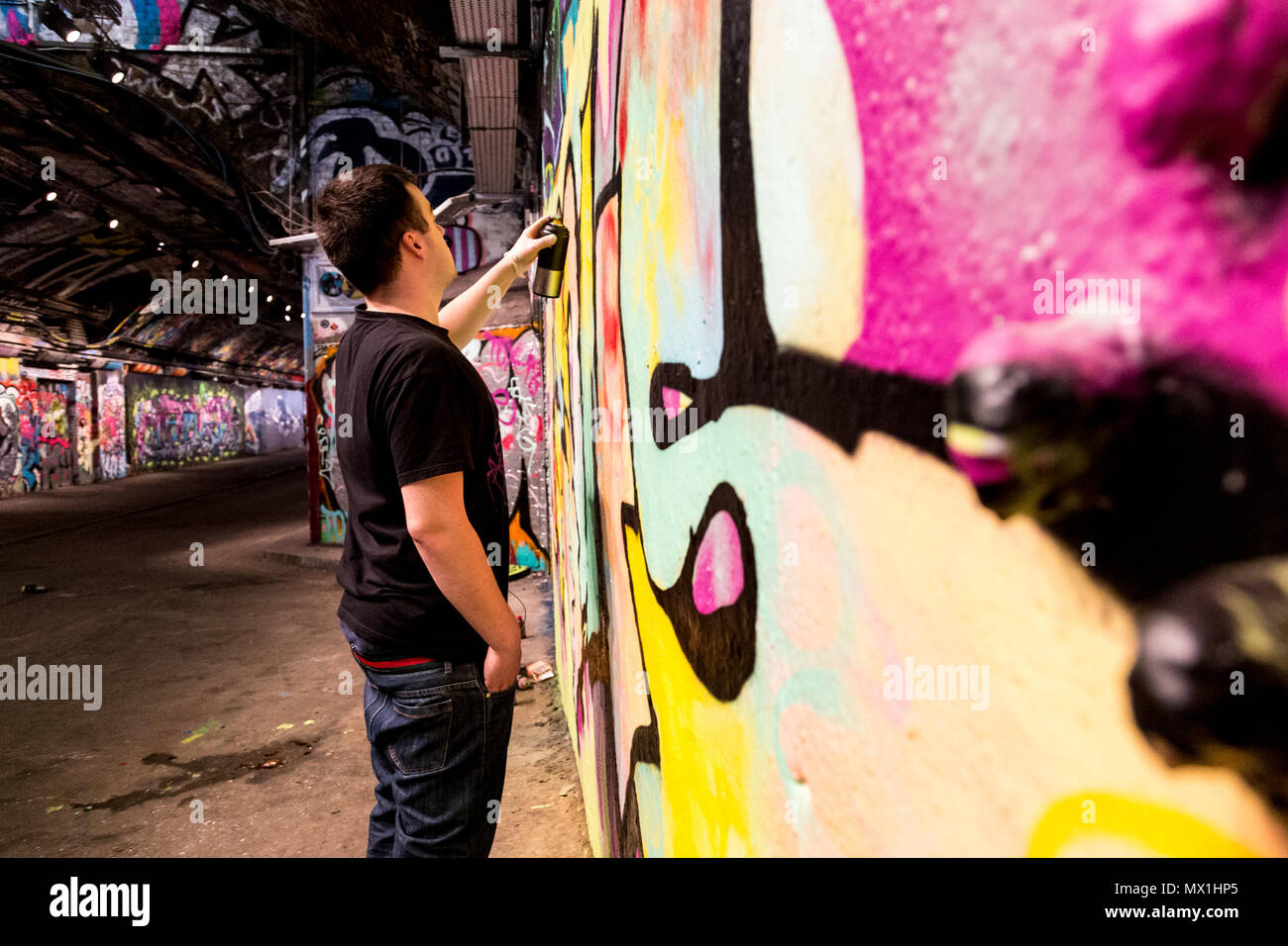 Londra, Regno Unito, 17 Aprile 2018: un uomo è al lavoro sul suo graffiti in una buia alee sotterraneo in un centro di Londra Waterloo. Foto Stock