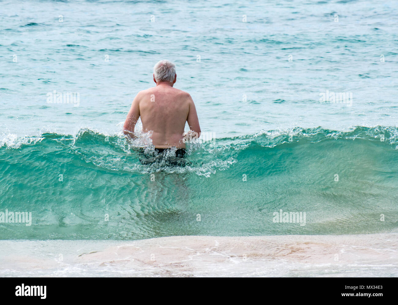 Senior uomo entrando in oceano, con wave rottura, Anakena, Isola di Pasqua, Rapa Nui, Cile Foto Stock