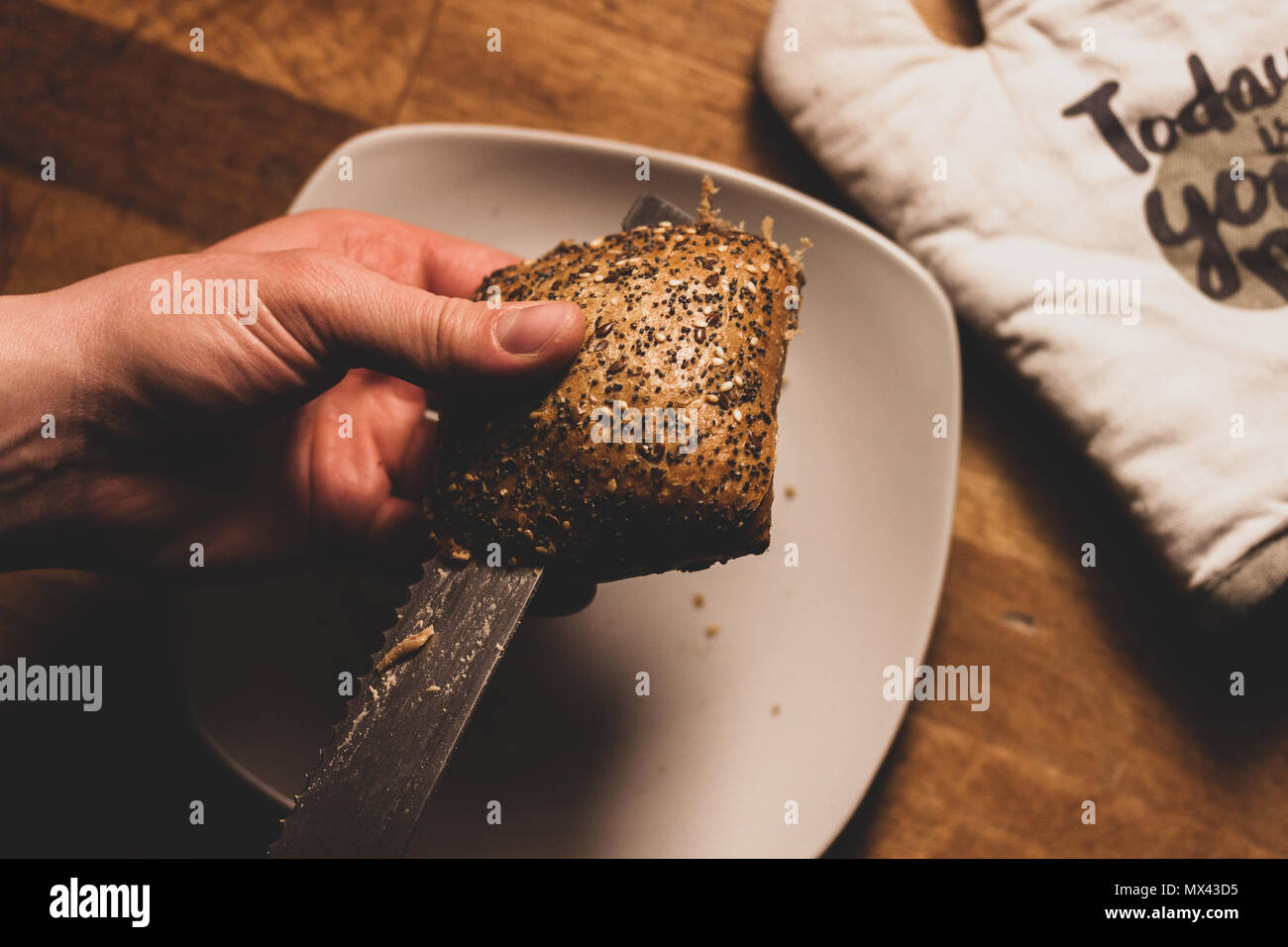 Un uomo di taglio di un pane integrale roll in cucina. Foto Stock
