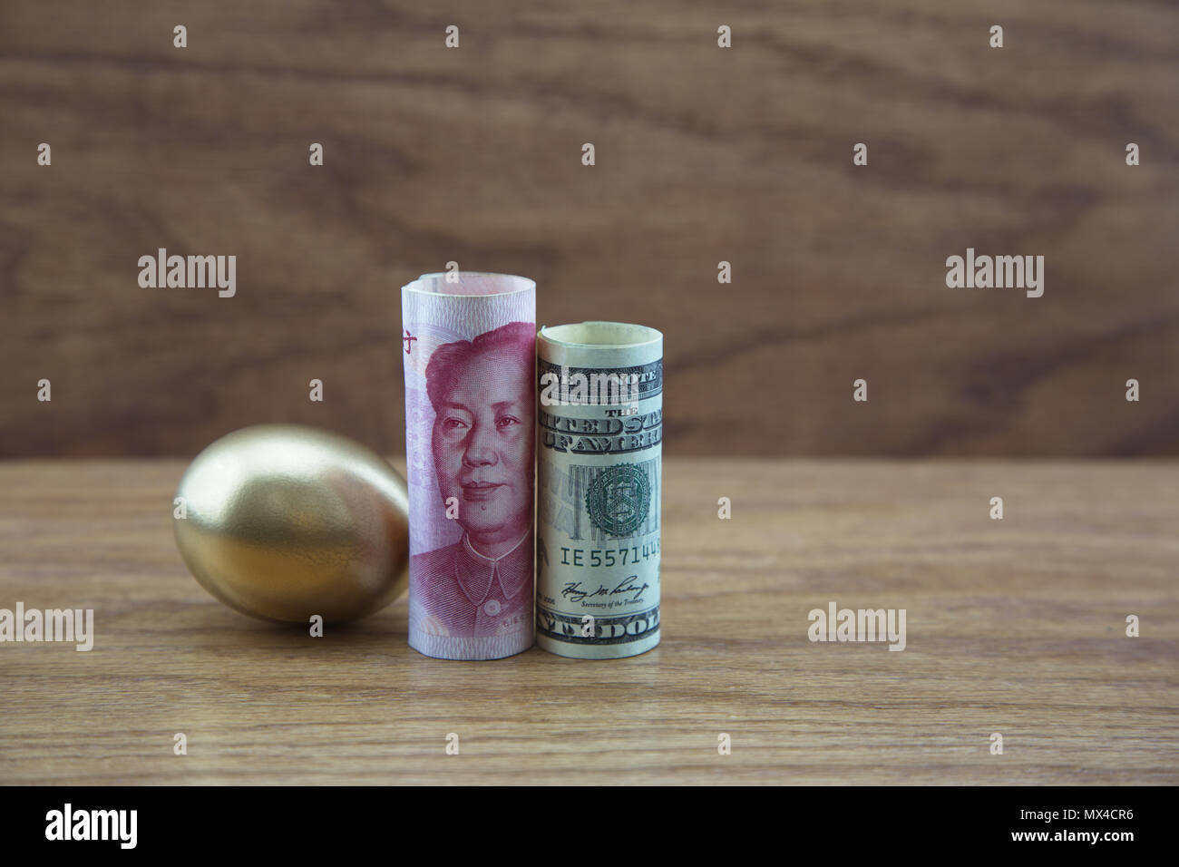Vantaggioso Americana e Pacific Rim investimenti simboleggiata in oro uovo con il dollaro e moneta yuan sofisticati contro uno sfondo di legno Foto Stock