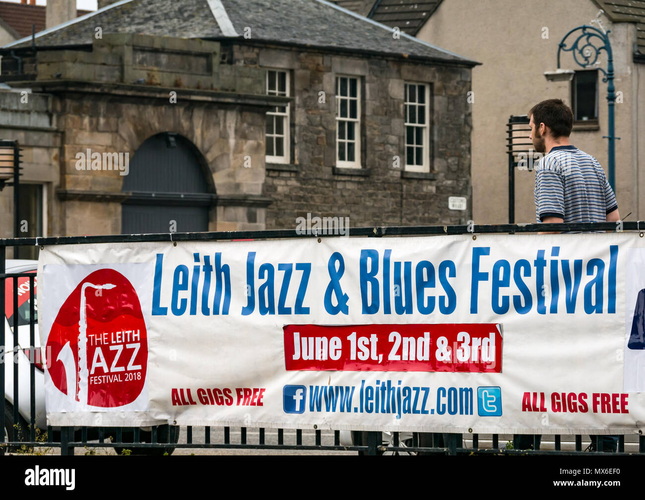 Leith Jazz & Blues Festival di musica dal vivo nei ristoranti e bar dall'acqua di Leith, 3° giugno 2018. La Riva, Leith, Edimburgo, Scozia, Regno Unito. Il jazz e blues festival si svolge su 3 giorni del fine settimana. Il festival banner visualizzati su un ponte sull'acqua di Leith con un uomo a camminare lungo una vecchia lampada ornati post Foto Stock