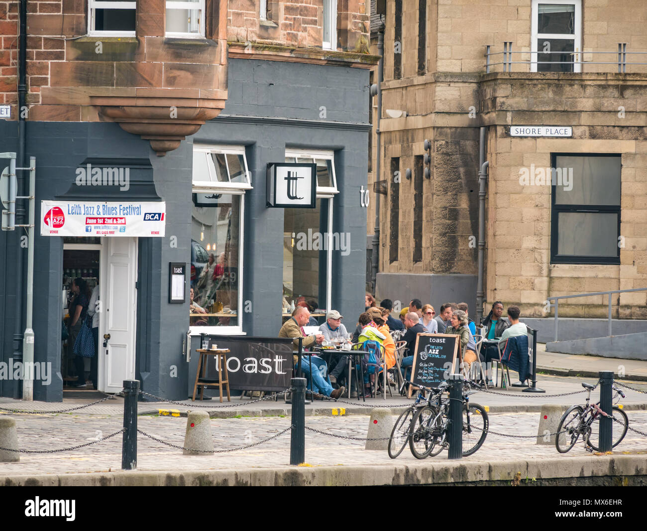 Leith Jazz & Blues Festival di musica dal vivo nei ristoranti e bar dall'acqua di Leith, 3° giugno 2018. La Riva, Leith, Edimburgo, Scozia, Regno Unito. Il jazz e blues festival si svolge su 3 giorni del fine settimana. Persone affollano il pavimento esterno tavoli di ristoranti e bar lungo l'acqua di Leith gode di ascoltare gratuitamente musica dal vivo. Persone presso il wine bar e ristorante chiamato Toast con il festival banner visualizzati Foto Stock