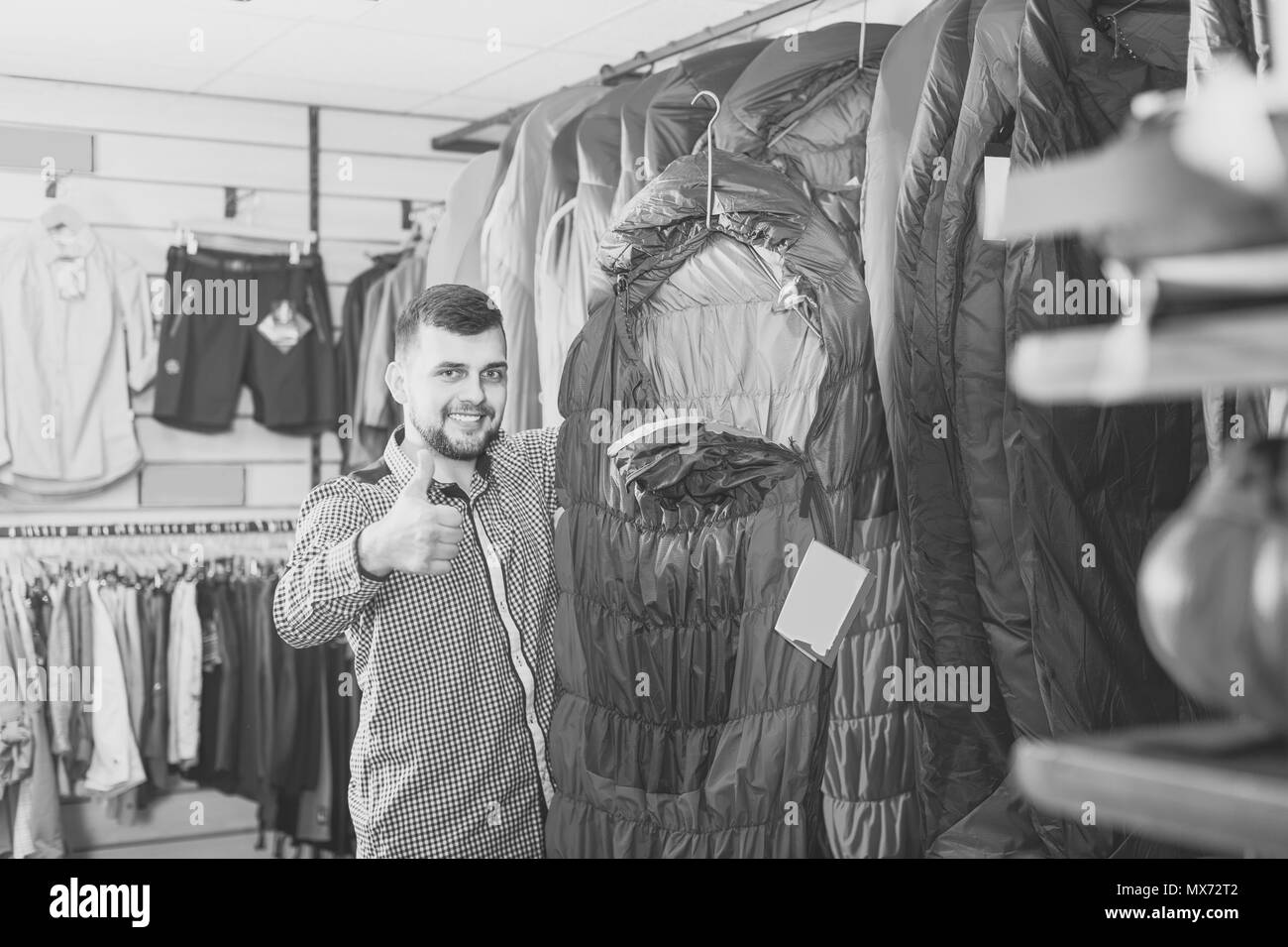 Giovane uomo scegliendo nuovo sacco a pelo in negozio per articoli sportivi Foto Stock