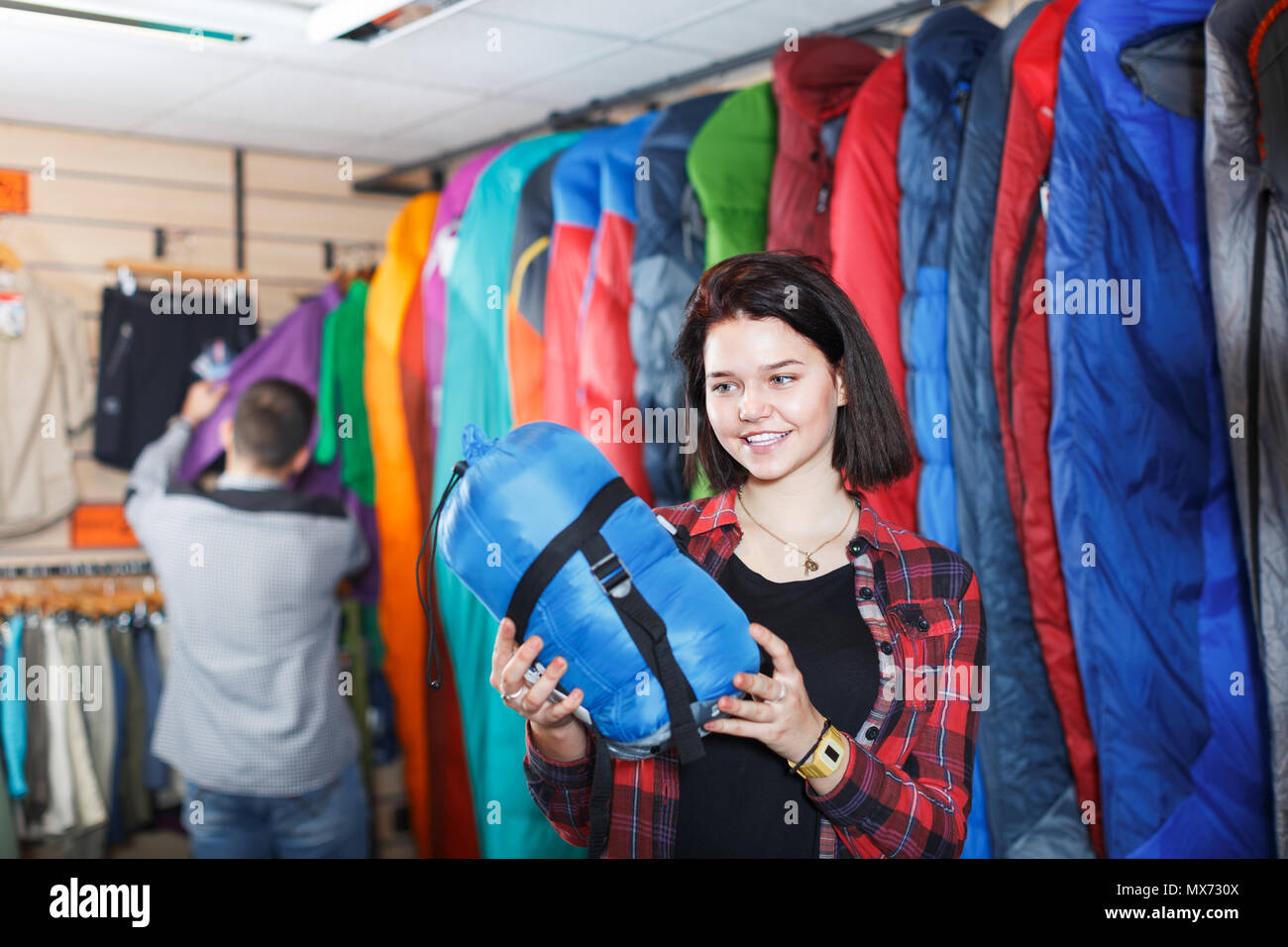 Giovane donna positiva di decidere sul nuovo sacco a pelo in negozio per articoli sportivi Foto Stock