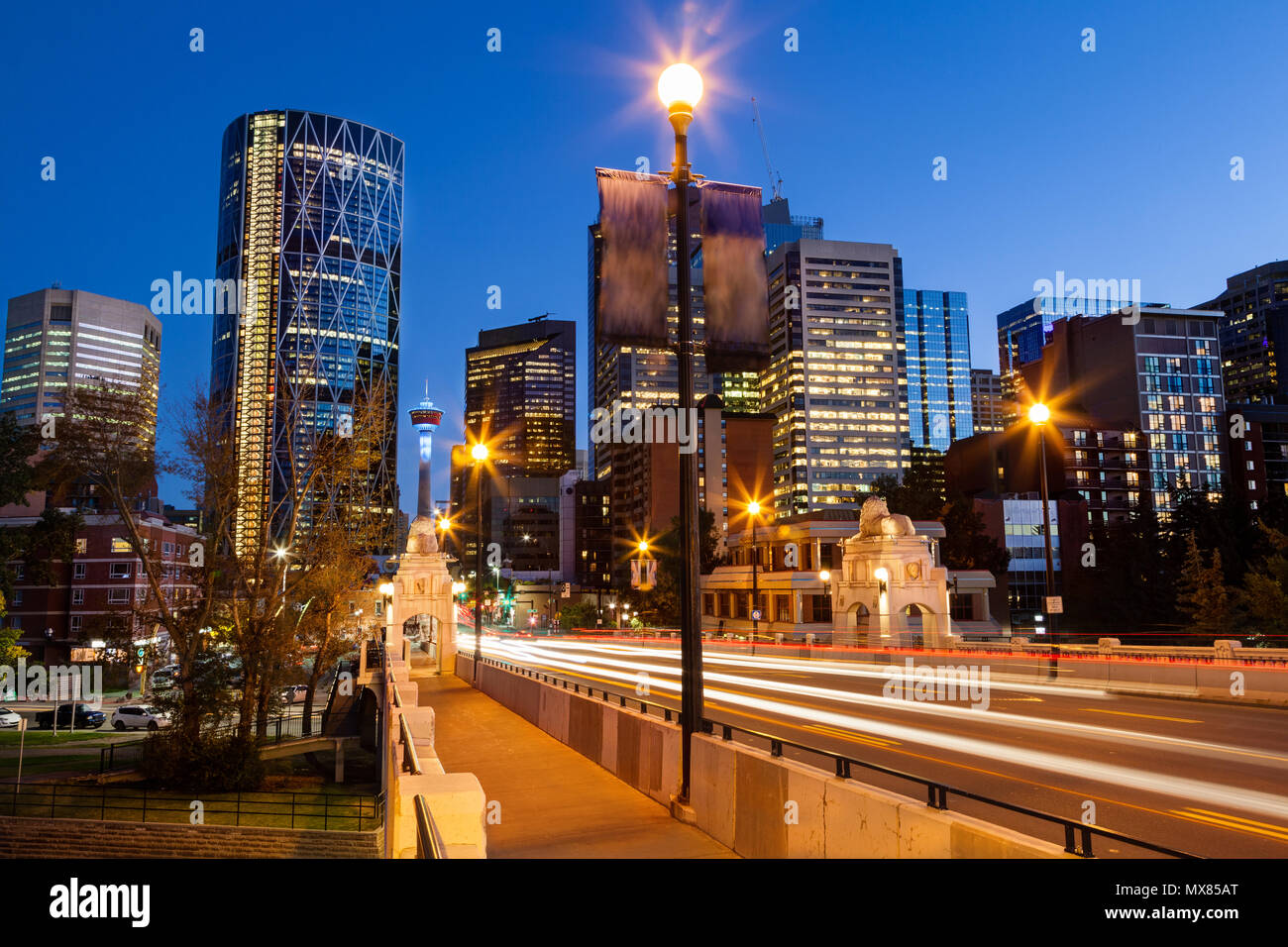 Sentieri di luce dal movimento vetture entrano Calgary quartiere finanziario del centro cittadino sulla strada del centro ponte che attraversa il Fiume Bow di notte tempo con la mitica C Foto Stock