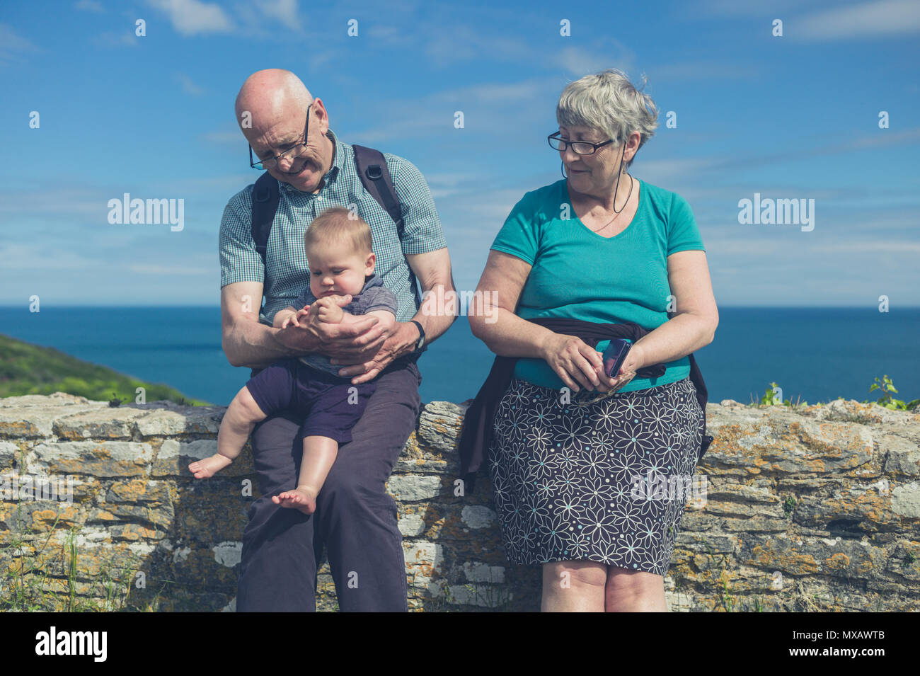 Una coppia di anziani è seduta su una parete dal mare con i loro nipoti Foto Stock