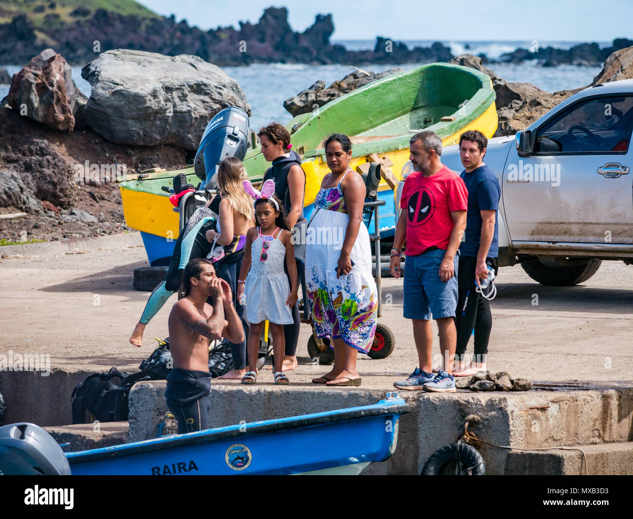 Uomo in wetsuit chiamando fuori dalla piccola barca in porto con la popolazione locale sulla banchina, Hanga Roa, Isola di Pasqua, Cile Foto Stock