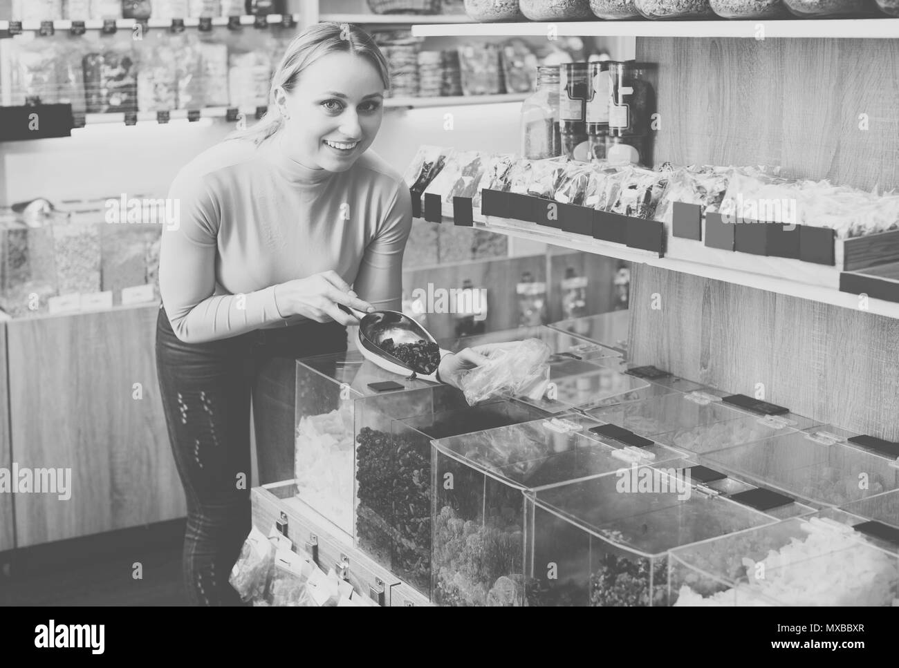 Giovane donna felice in piedi accanto a contenitori con frutti di bosco essiccati e la raccolta selezionata nel negozio organico Foto Stock