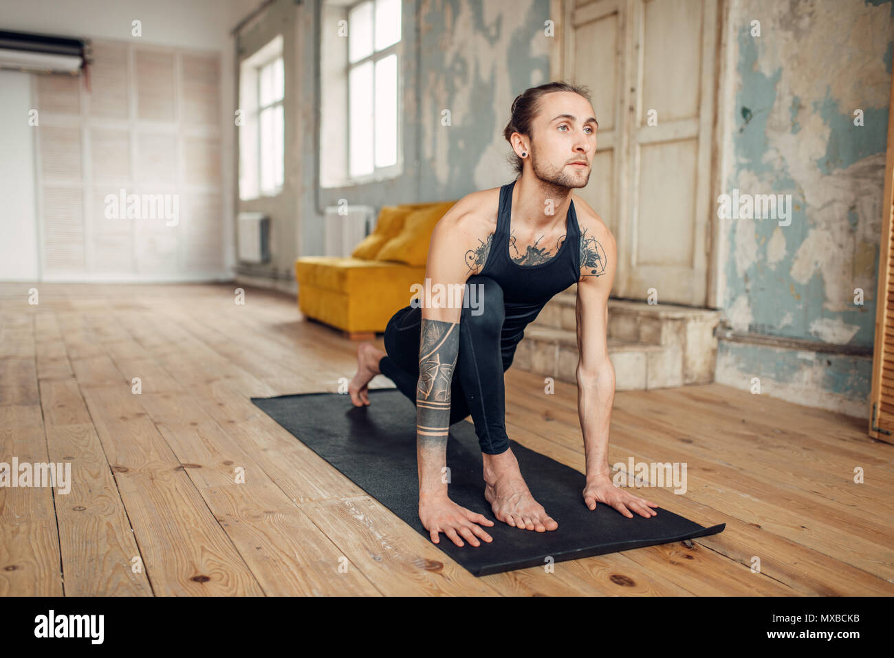 Yoga maschio con tatuaggio sul lato fare esercizio in palestra con grunge interni. Allenamento di fitness in ambienti interni Foto Stock
