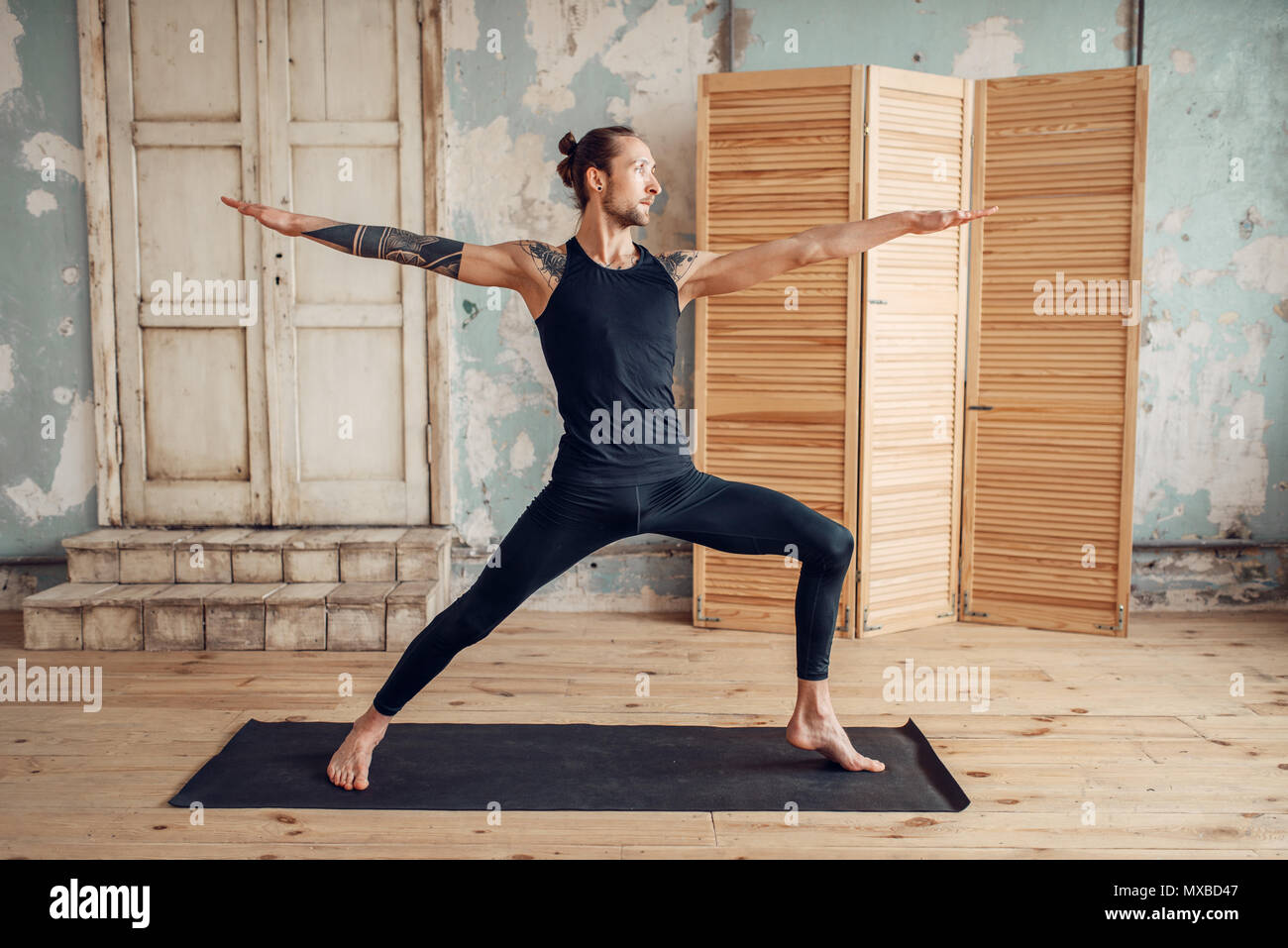 Yoga maschio con tatuaggio sul lato facendo stretching esercizio sul tappeto in palestra con grunge interni. Montare l'allenamento al chiuso Foto Stock